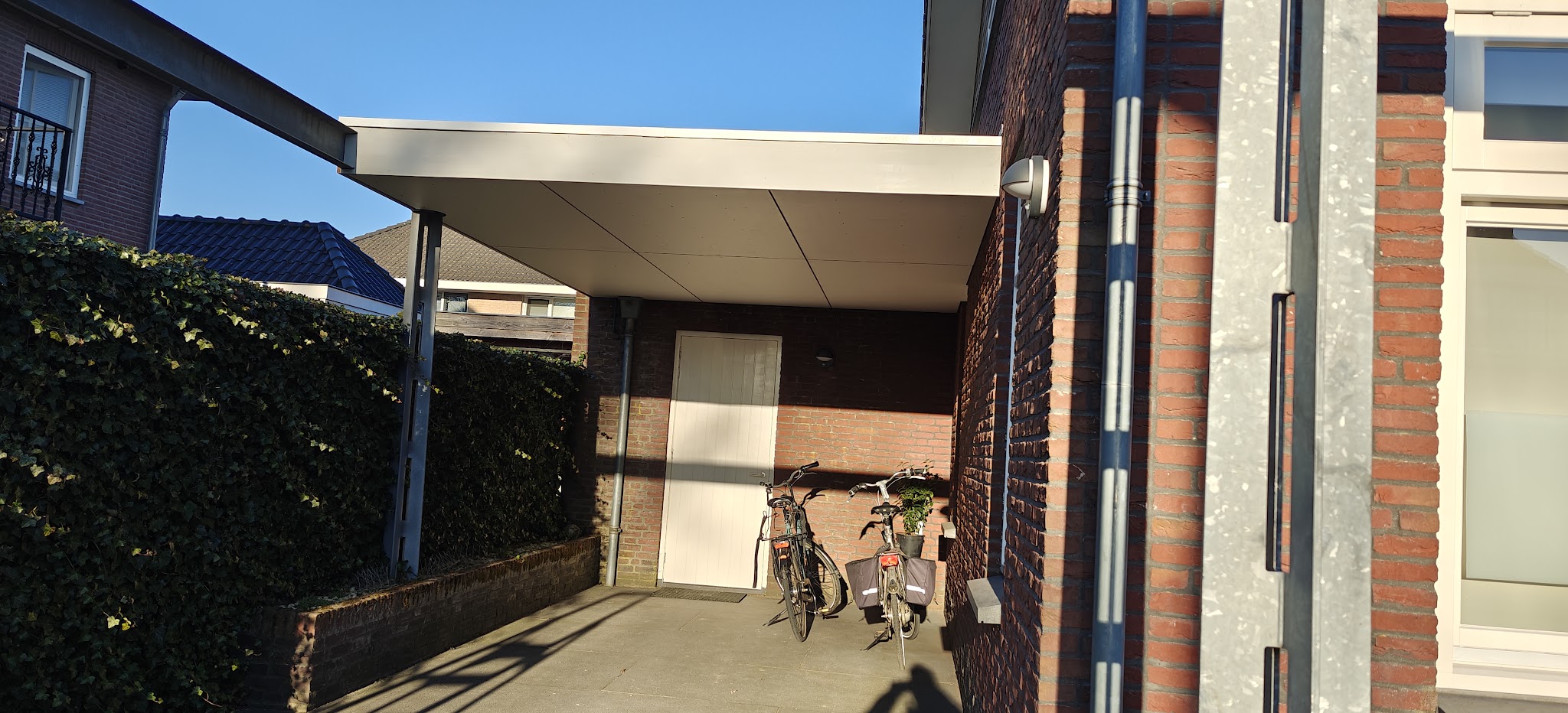Wit afdak met plat dak tussen twee bakstenen huizen, fietsen eronder