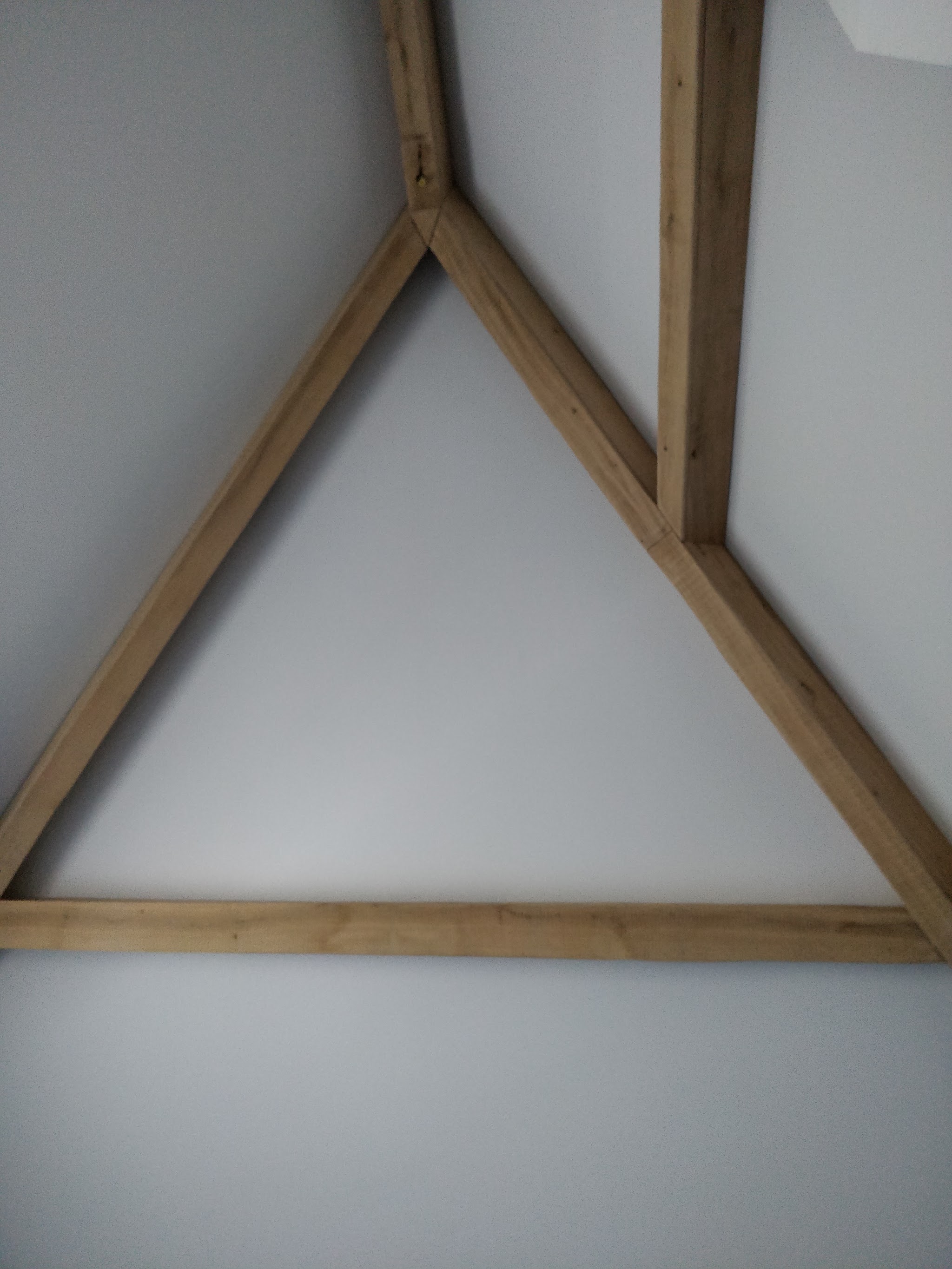 Houten dakspant in driehoeksvorm tegen een wit plafond, van onderaf gezien